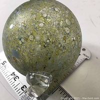 Glass ball on measuring tape showing approx. 4.5 inch diameter and attached clear hanging loop.