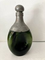 Green glass decanter with matte metal stopper and cover, showing full height and bulbous green glass body.