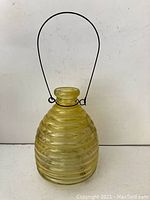 Yellow vintage glass wasp jar with wire handle photographed against white background.