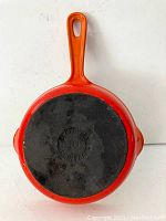 Bottom of orange Le Creuset skillet showing black cast iron base with Le Creuset logo and size 16 stamped.