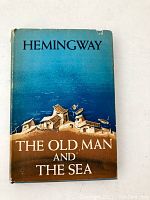 Front view of dust jacket featuring illustration of small seaside houses under title 'THE OLD MAN AND THE SEA' and author 'HEMINGWAY'