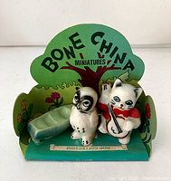 Close up of the miniature nursery rhyme Owl and Pussycat bone china figurines with accompanying green accessory and backdrop