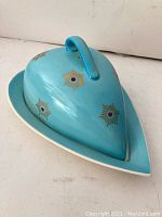 Side angle of the closed heart-shaped covered dish, showing light blue glaze and gold/red star decoration.