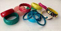 Group photo of all 13 vintage plastic bangles in various colors and designs on white background.