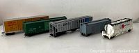 Five toy train cars in a lineup, featuring varied railroad branding including Union Pacific and BC Railway.