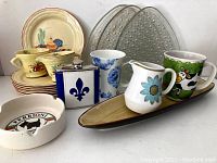 Full view of lot: various ceramic ashtrays, dishes, cups, a flask, and trays in multiple colors and designs