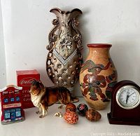 Photo showing all nine decorative items including two vases, ceramic Collie dog figurine, Coca Cola collectibles (building, can, box), four decorated eggs, and small clock on white background.