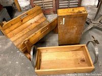 Wood log holder with curved wooden slats and metal handles visible, two wooden boxes stacked beside it in basement setting.