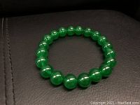 Green jade beaded bracelet laid flat on dark surface, showing round polished beads forming a circular shape.