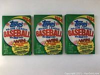 Three unopened 1984 Topps Major League Baseball card packs with promotional front design, displayed flat.