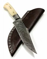 Photo showing the full Damascus blade with bone handle resting on the leather sheath, highlighting the Damascus pattern and bone rivets.