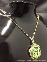 Green jade pendant with gold dragon mount on a gold chain displayed on a black mannequin bust from a front angle.