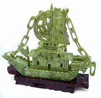 Front-left angled view showing detailed carving of ship, sail, wheel, and chain links mounted on wooden base.