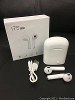 Photo of white i7S-TWS earbuds, charging case, USB cable and box on black background.