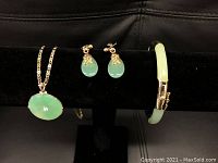 Full view of the 4 piece jewelry set displayed on black stand: necklace with round jade pendant, pair of jade earrings, and jade bangle.