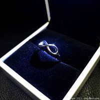 Close-up image of a ladies 925 sterling silver infinity ring in a black velvet-lined white jewelry box.