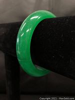 Front and side views of green jade carved ladies bangle bracelet displayed on black velvet stand, showing smooth polished finish and translucent green color.