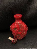 Front view of an Asian red cinnabar carved snuff bottle depicting a peacock and floral motifs with detached stopper.