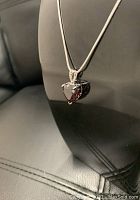 Close-up photo of heart-shaped garnet gemstone pendant on silver plated snake link chain, showing the deep red color of the gemstone and silver setting.