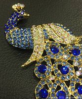 Front close-up of large gold-tone peacock brooch with royal blue and other colored rhinestones on black background.