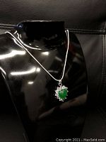 Mounted green jade heart shaped pendant with silver detailing on a 925 sterling silver snake link necklace displayed on a black mannequin bust