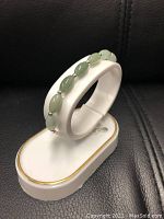 Natural oval green jade bangle bracelet displayed on a white jewelry holder.