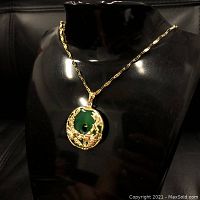 Front view of the gold plated necklace with a green jade pendant featuring dragon and phoenix design, displayed on a black bust.