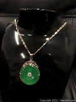 Front side of the green jade circular pendant featuring a central sparkling gemstone attached to an 18K gold plated necklace chain.