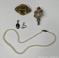 Photo showing entire lot with faux pearl necklace, blue stone pendant, faux pearl earring, brass floral brooch, and marcasite flower brooch.
