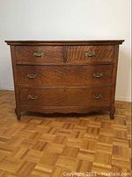 Front view of the antique oak dresser showing all four drawers, brass pull handles, and keyholes. The dresser is on parquet flooring.