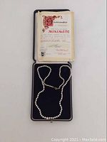 Necklace laid in open presentation case with guarantee certificate visible