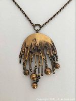 Close-up front view of bronze pendant showing dripping design with five spherical dangles.