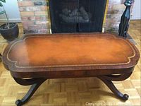 Full front view of vintage leather top coffee table showing rectangular top and curved wooden legs.