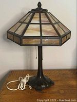 Full view of antique table lamp showing heavy metal base, stained glass shade, and pull chain switch on wooden surface