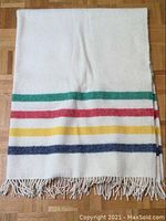 Folded view showing off-white wool with green, red, yellow, navy stripes and twisted fringe