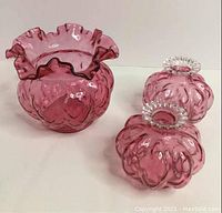 Set of three cranberry glass vases shown on white surface. One large vase with ruffled rim and two smaller vases with clear circular mouths.