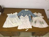 Four vintage baby clothing items: blue pea coat and three spring dresses laid flat