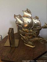 Photo showing detailed side view of brass boat lamp with ship sails and figures, alongside one brass bookend.