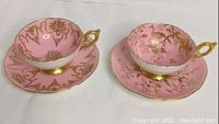 Front view of two pink and gold tea cups on matching saucers.