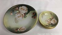 One photo showing one large bowl on left with floral design and five smaller bowls stacked on right with same design.