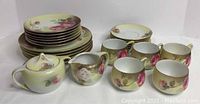Complete partial luncheon set arranged showing 5 teacups, 6 saucers, 6 dessert plates, 5 lunch plates, sugar bowl, and creamer jug with floral pink rose design on yellow and gold background.