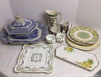 Wide view showing all items including large platter, covered dish, plates, cream and sugar bowls, and jug on a white surface.