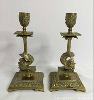 Pair of brass koi fish and sea serpent themed candle holders with square floral ornate bases, shown from the front.