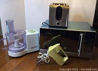 Photo shows all four appliances together: microwave, toaster on top, food processor to left, hand mixer in front.