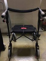 Front angled view showing walker frame, wheels, padded seat, backrest and handrails with ergonomic plastic handles and brake levers.