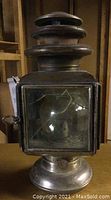 Full view of the antique metal lantern showing the tarnished metal body and cracked front glass panel.
