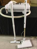 Canister vacuum with connected hose and extension wands standing upright next to attachments