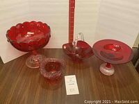 Four different decorative red glass candy dishes arranged on a wood surface with measurement scale in background.