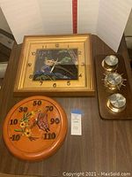 Photo showing wall clock with gold frame and floral black face, ceramic wall thermometer with floral and butterfly relief design, and three-gauge weather station with brass color.