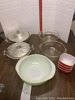 Complete set of Pyrex dishes including yellow casserole, clear casserole dishes, four small red square dishes, along with two covered metal serving dishes.